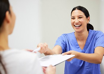 Dental assistant smiling while handing patient form