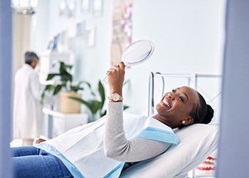 Woman smiling at reflection in mirror while sitting in treatment chair