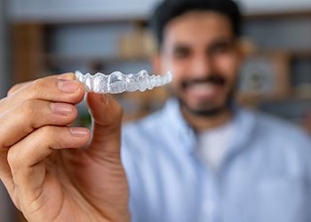 Man smiling while holding up Invisalign aligner