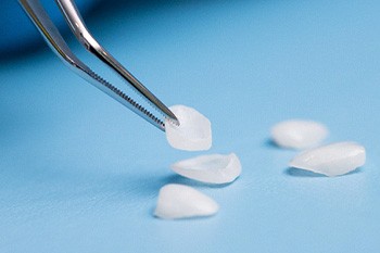 A dentist holding a porcelain veneer with tweezers