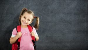 little girl with pigtails standing in front of black chalkboard 