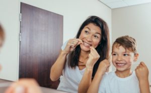 young boy flossing teeth following mom's example